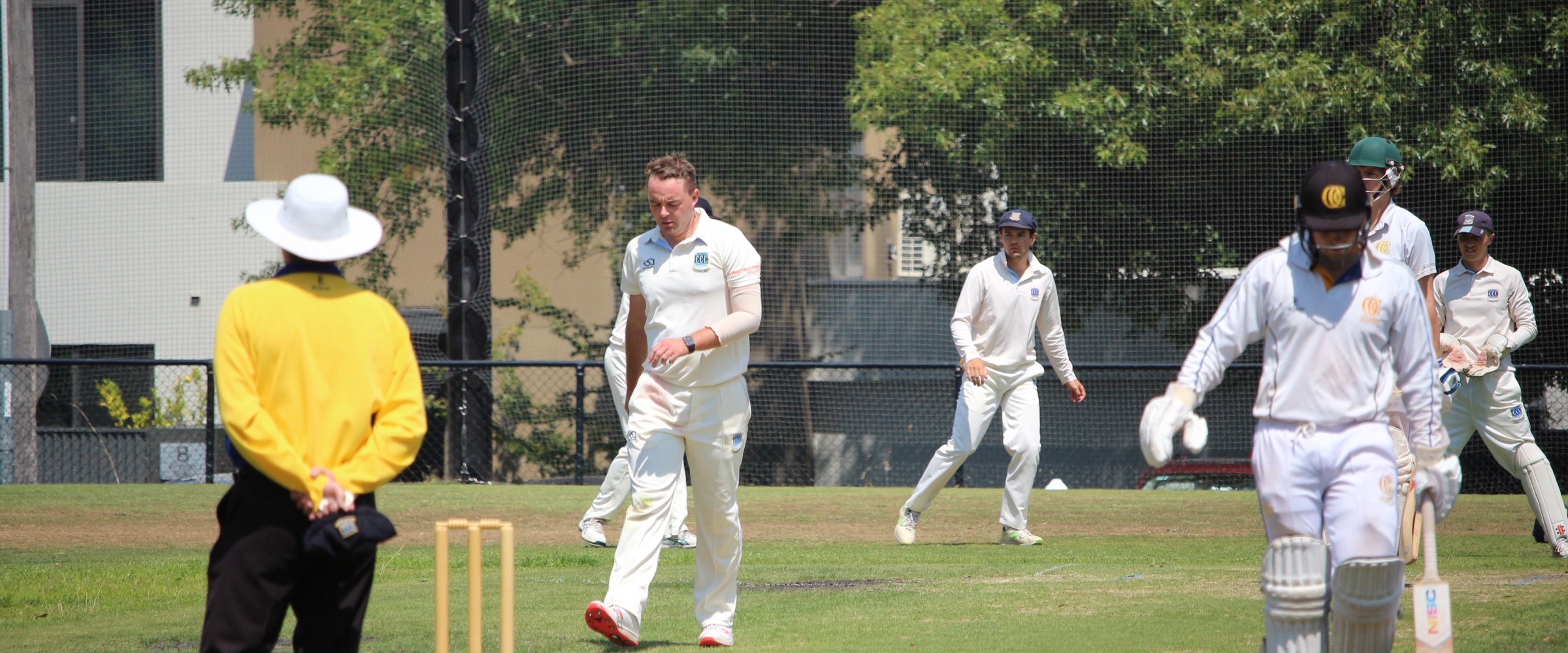 A Canterbury bowler walks back to his mark at Canterbury Sports Ground as the batters complete a run, fielders spread behind him