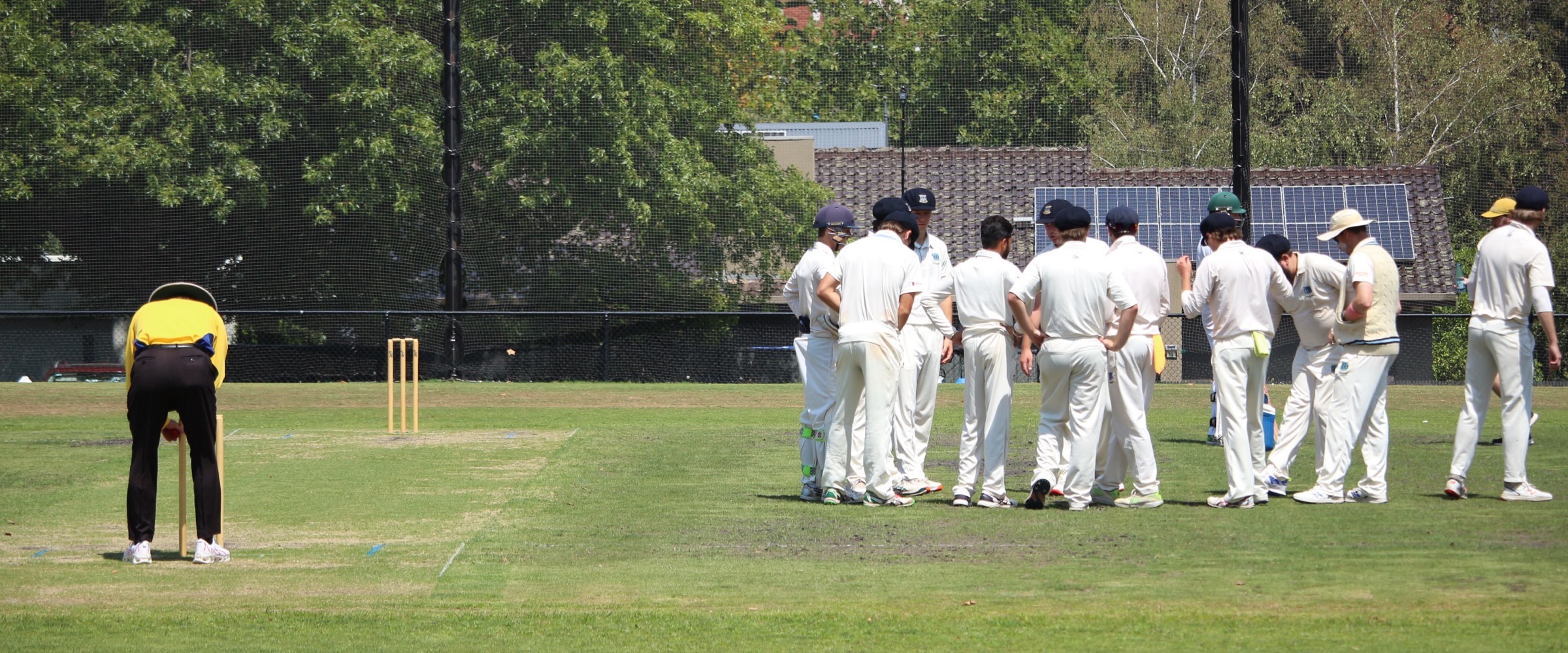The Canterbury fielding side gathered together between overs at Canterbury Sports Ground, the umpire waiting at the stumps