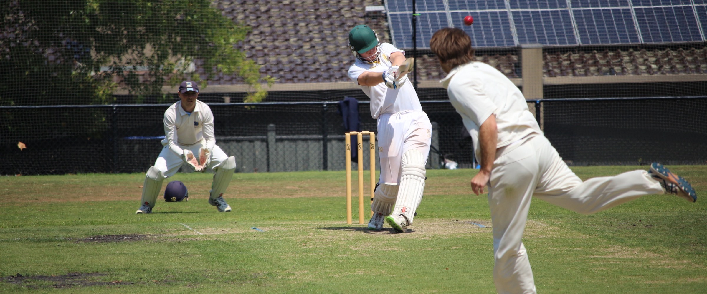 An opposition batter pulls a short ball square on the turf at Canterbury Sports Ground, the Canterbury wicketkeeper crouched behind the stumps and the bowler following through