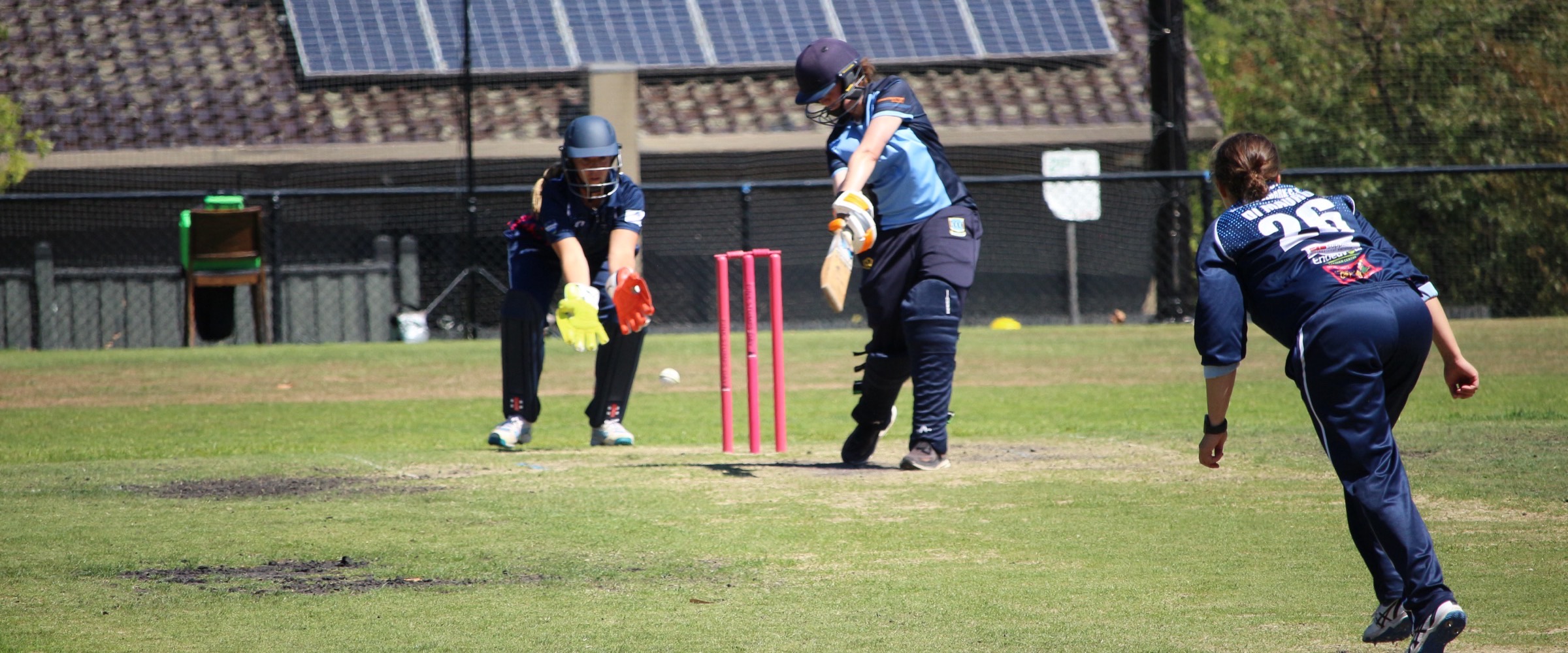 A Canterbury batter plays a shot past the pink stumps on Pink Stumps Day, the wicketkeeper crouched with gloves ready and the bowler following through